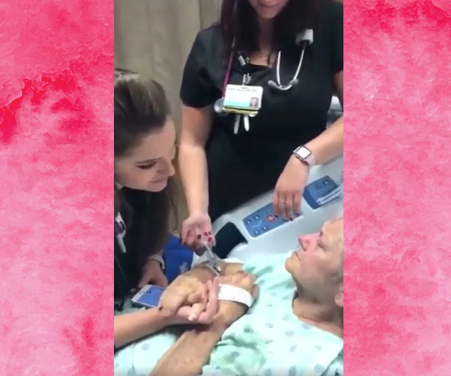 Nurse holding a patient's hand, singing to her as another nurse stands by the hospital bed.