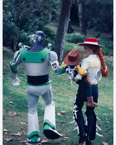 Family dressed as Buzz Lightyear, Jessie, and Woody from Toy Story walking in a park.