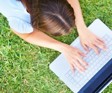 Person lying on grass using a laptop outdoors, viewed from above.