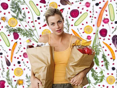 Woman holding grocery bags with a colorful vegetable background, including carrots, radishes, and cucumbers.