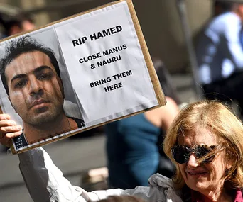 Woman holding a protest sign with a photo labeled "RIP Hamed," urging to close Manus & Nauru refugee centers.