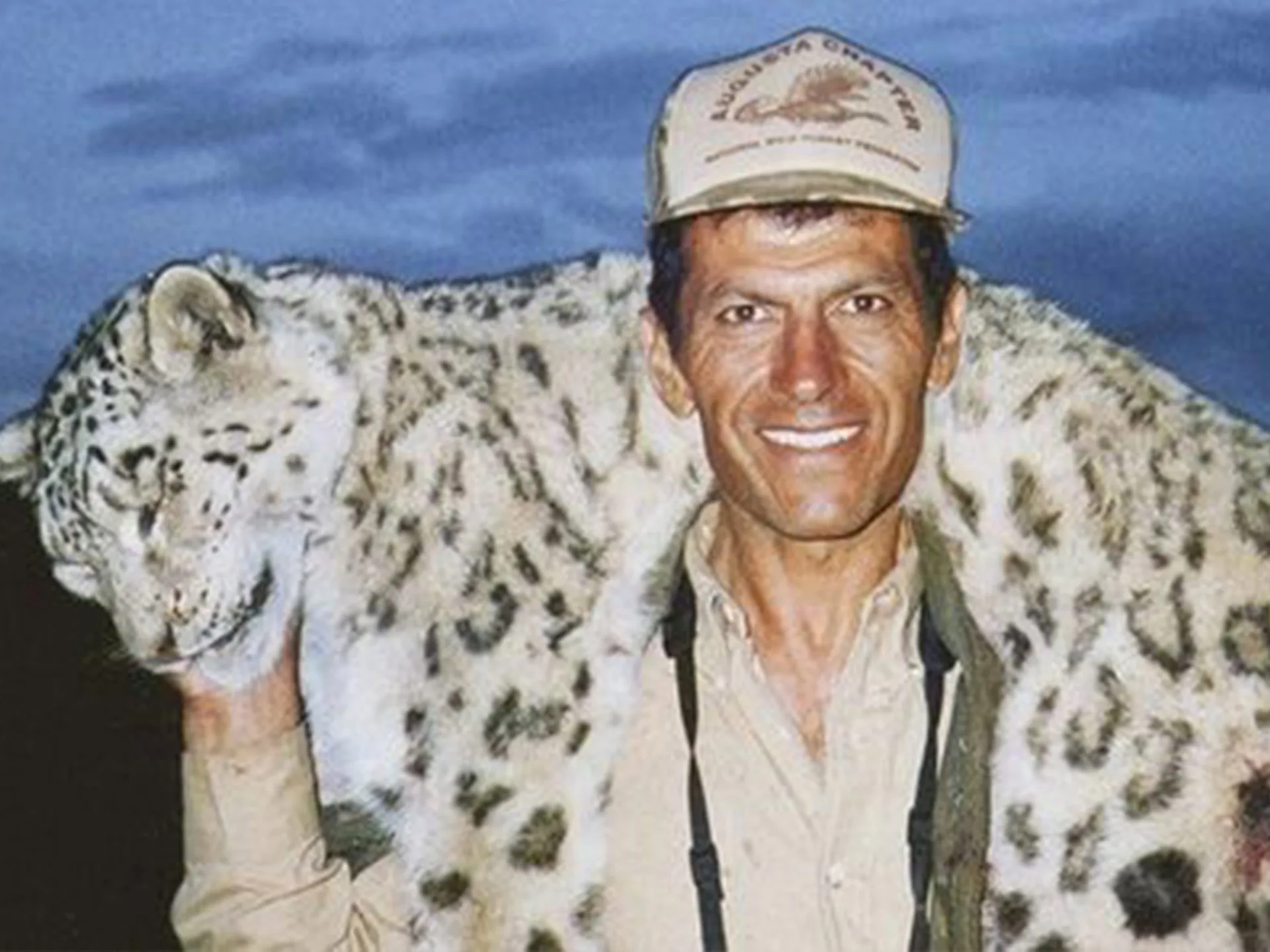 Man smiling while holding a snow leopard carcass over his shoulders.