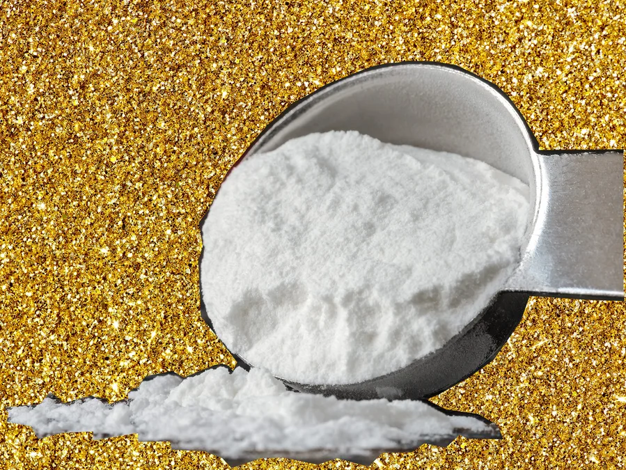 Scoop of baking soda against a gold glitter background.