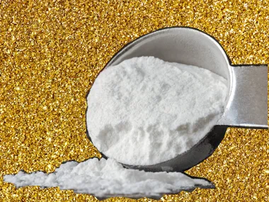 Scoop of baking soda against a gold glitter background.