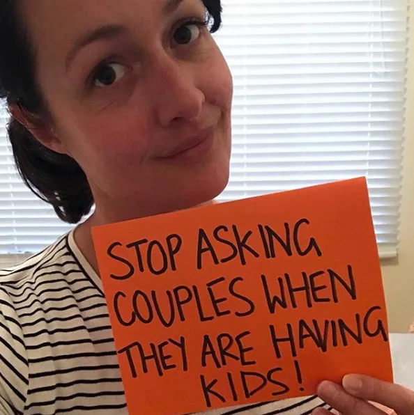 Woman holding a sign that says, "Stop asking couples when they are having kids!"
