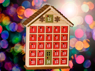 Wooden advent calendar with 25 numbered red doors resembling a house, with a colorful bokeh background.