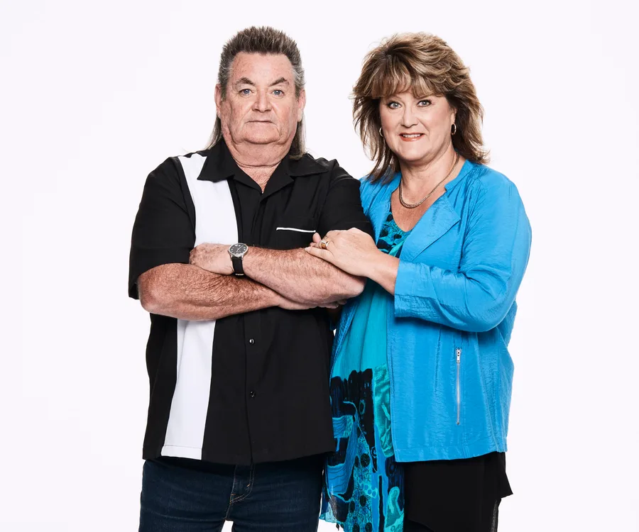 A couple from "Instant Hotel," dressed casually, pose together against a white background.