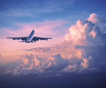 Airplane flying into sunset skies above fluffy clouds.