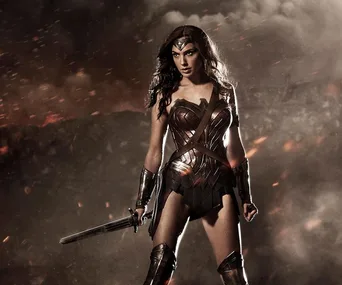 Wonder Woman in battle armor stands in a smoky, fiery landscape, holding a sword.
