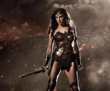 Wonder Woman in battle armor stands in a smoky, fiery landscape, holding a sword.