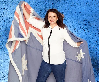 Australian politician Jacqui Lambie stands smiling, holding an Australian flag against a blue background.