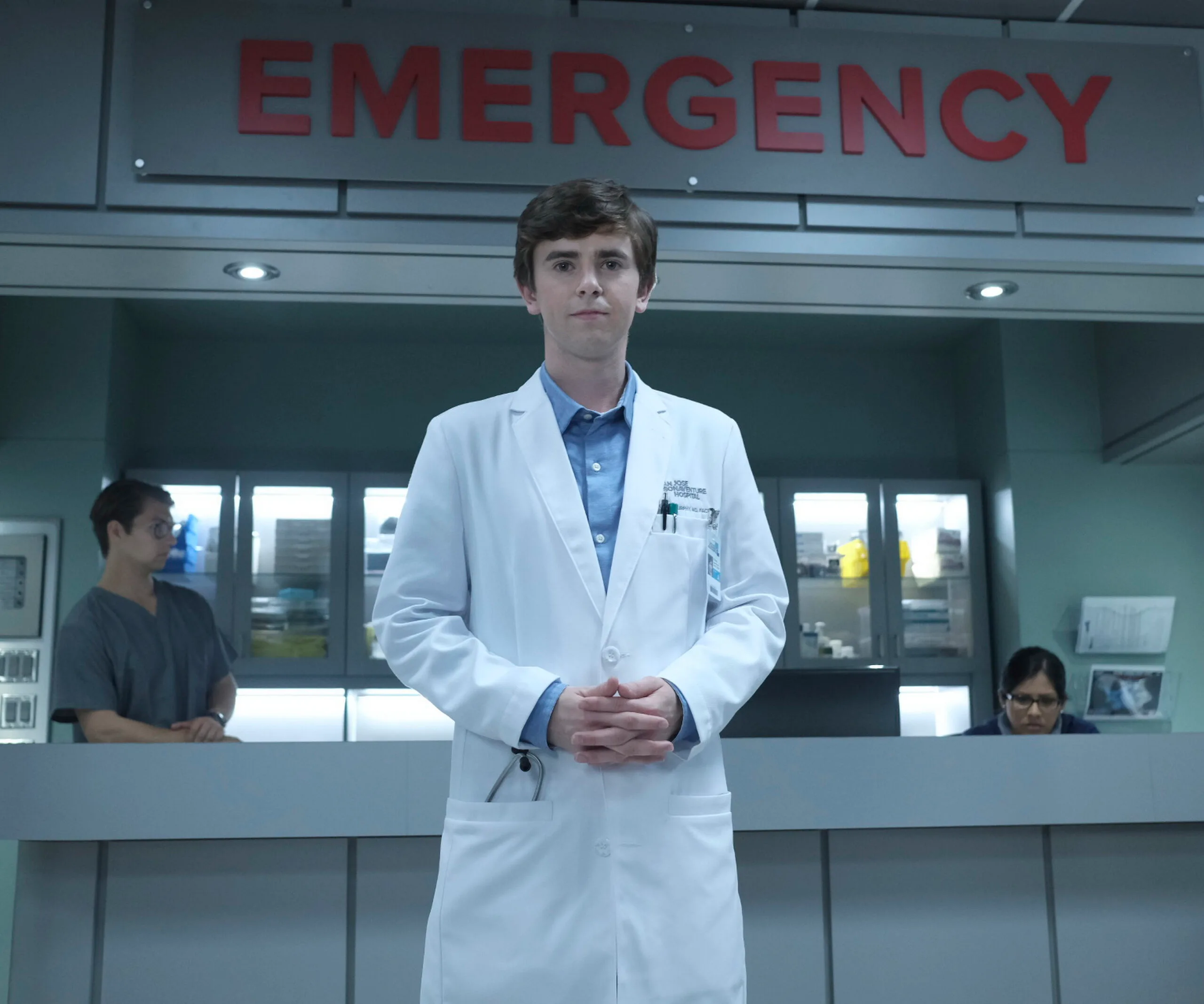 Dr. Shaun Murphy, in a white coat, stands in a hospital emergency room from "The Good Doctor."