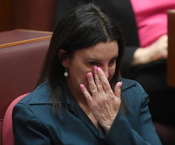 A person in teal clothing wipes tears during an emotional moment in a formal setting.