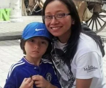 Mother smiling and hugging a young boy wearing a blue cap and jersey, with a carriage wheel in the background.