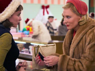 Two women in vintage clothing talking in a store, one holding a purse, with holiday decorations in the background.