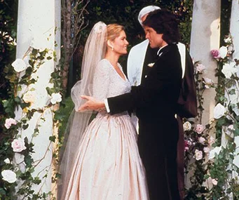 Bride and groom embracing at an outdoor wedding altar adorned with pink and white roses.