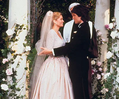 Bride and groom embracing at an outdoor wedding altar adorned with pink and white roses.