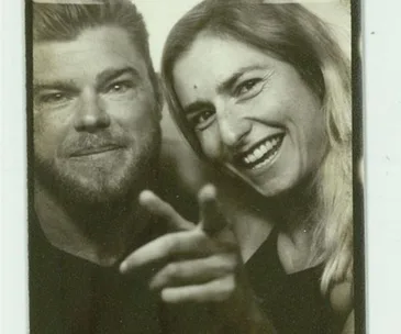 A smiling couple in a close-up black-and-white photo, with the man pointing at the camera.