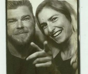 A smiling couple in a close-up black-and-white photo, with the man pointing at the camera.
