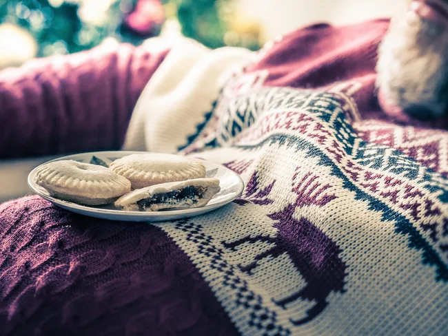 Plate of pastries on a festive sweater with reindeer design, blurred Christmas tree lights in the background.