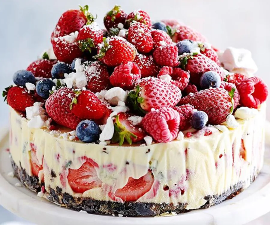 A Christmas ice cream cake topped with strawberries, raspberries, blueberries, and powdered sugar on a white platter.
