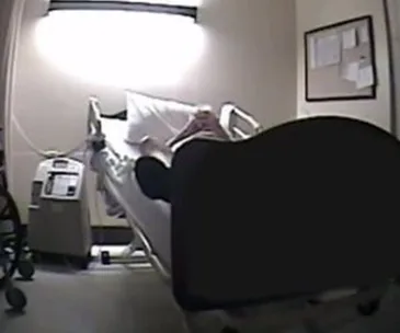 A patient lies in a hospital bed in a dimly lit room with medical equipment nearby.