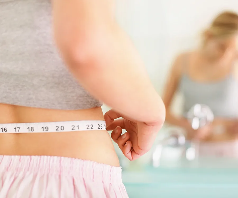 Person measuring waist with tape measure in front of mirror, highlighting body shape change.