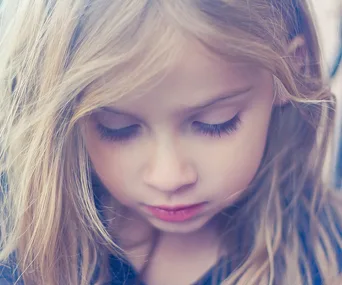 Young girl with long blonde hair looking down, expressing thoughtfulness or sadness.