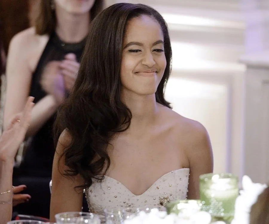 A young woman in a strapless dress smiles slightly at a formal event.