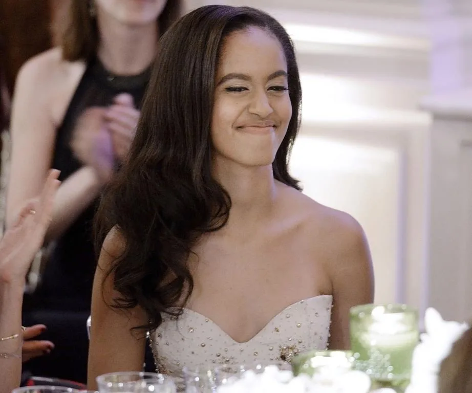 A young woman in a strapless dress smiles slightly at a formal event.