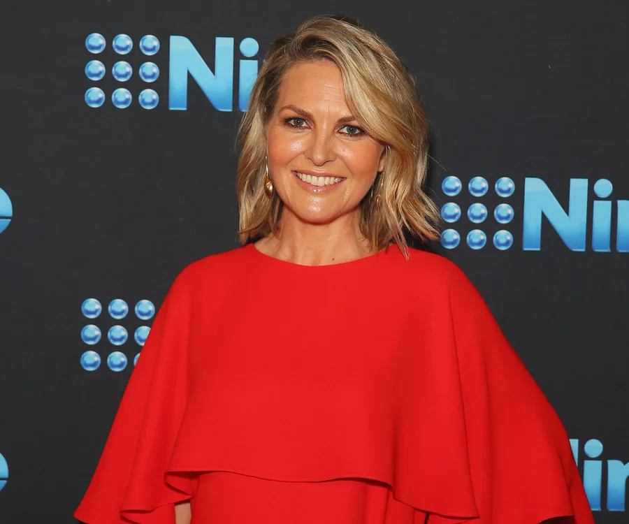 Person in a red dress smiling at a Nine Network event backdrop.