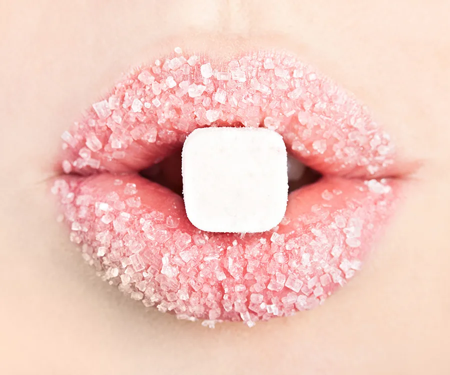 Close-up of lips coated in sugar with a sugar cube held between them.