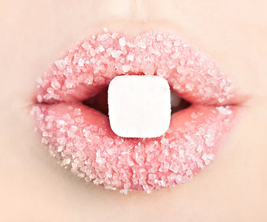 Close-up of lips coated in sugar with a sugar cube held between them.
