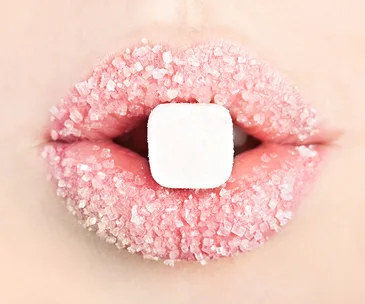 Close-up of lips coated in sugar with a sugar cube held between them.