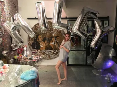 A woman posing in front of silver balloons spelling "Miley" in a decorated room.