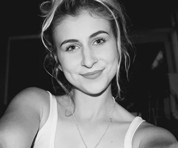 A young woman takes a black-and-white selfie, smiling softly, with a headband in her hair.