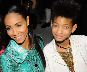 A woman in a green snakeskin jacket poses with a young girl in a white studded jacket, both smiling at an event.