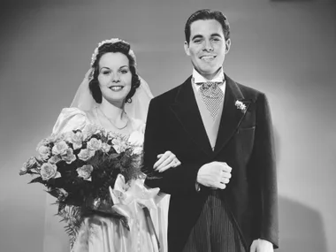 Black and white photo of a smiling bride and groom, the bride holding a bouquet of flowers.