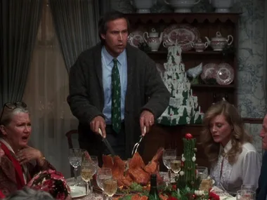 Man carving turkey at Christmas dinner table, family around looking surprised.