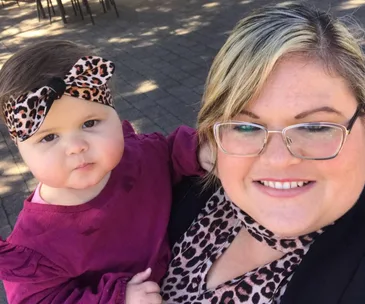 A smiling woman holds a baby with a leopard print headband, both wearing matching outfits.