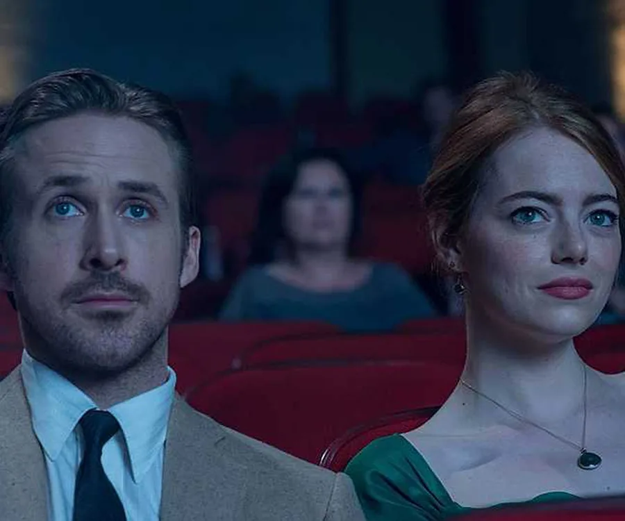 A man and woman sit together in a theater, looking ahead pensively.