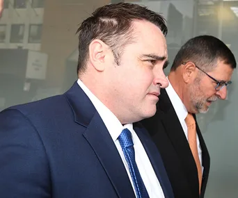Two men in suits walking outside a building, one with a blue tie and the other with an orange tie.