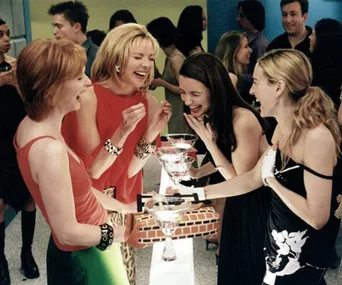 Four women laughing and holding martini glasses at a lively party.