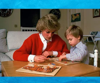 A woman and a young boy work on wooden puzzles together at a table in a cozy living room setting.
