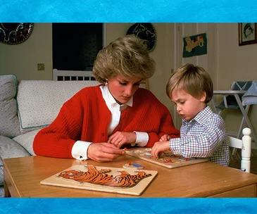 A woman and a young boy work on wooden puzzles together at a table in a cozy living room setting.