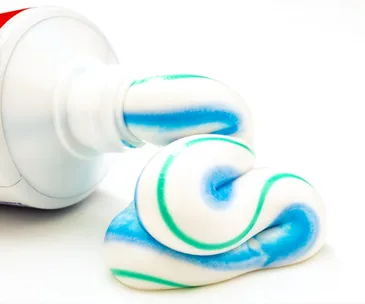 Toothpaste being squeezed from a tube, showing its blue and green stripes on a white background.