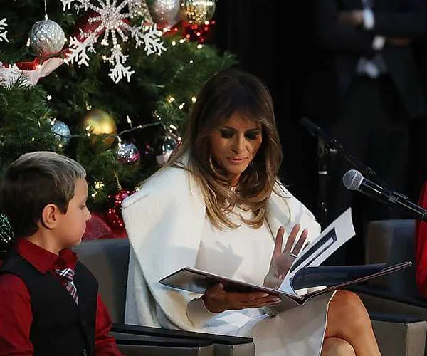 Melania Trump reads a book to children by a decorated Christmas tree.
