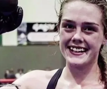 A young woman in a gym smiling after a workout, wearing exercise attire.