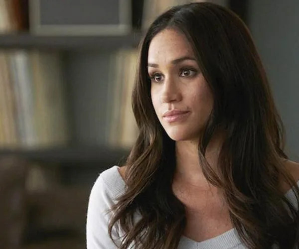 Meghan Markle as Rachel Zane in "Suits," wearing a white top, with a thoughtful expression in an office setting.