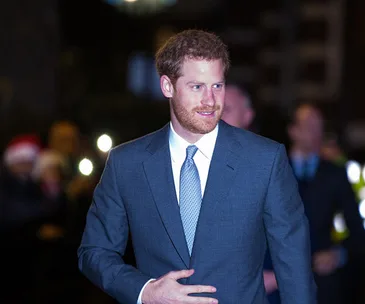 Prince Harry in a suit at a formal event, walking with a slight smile.